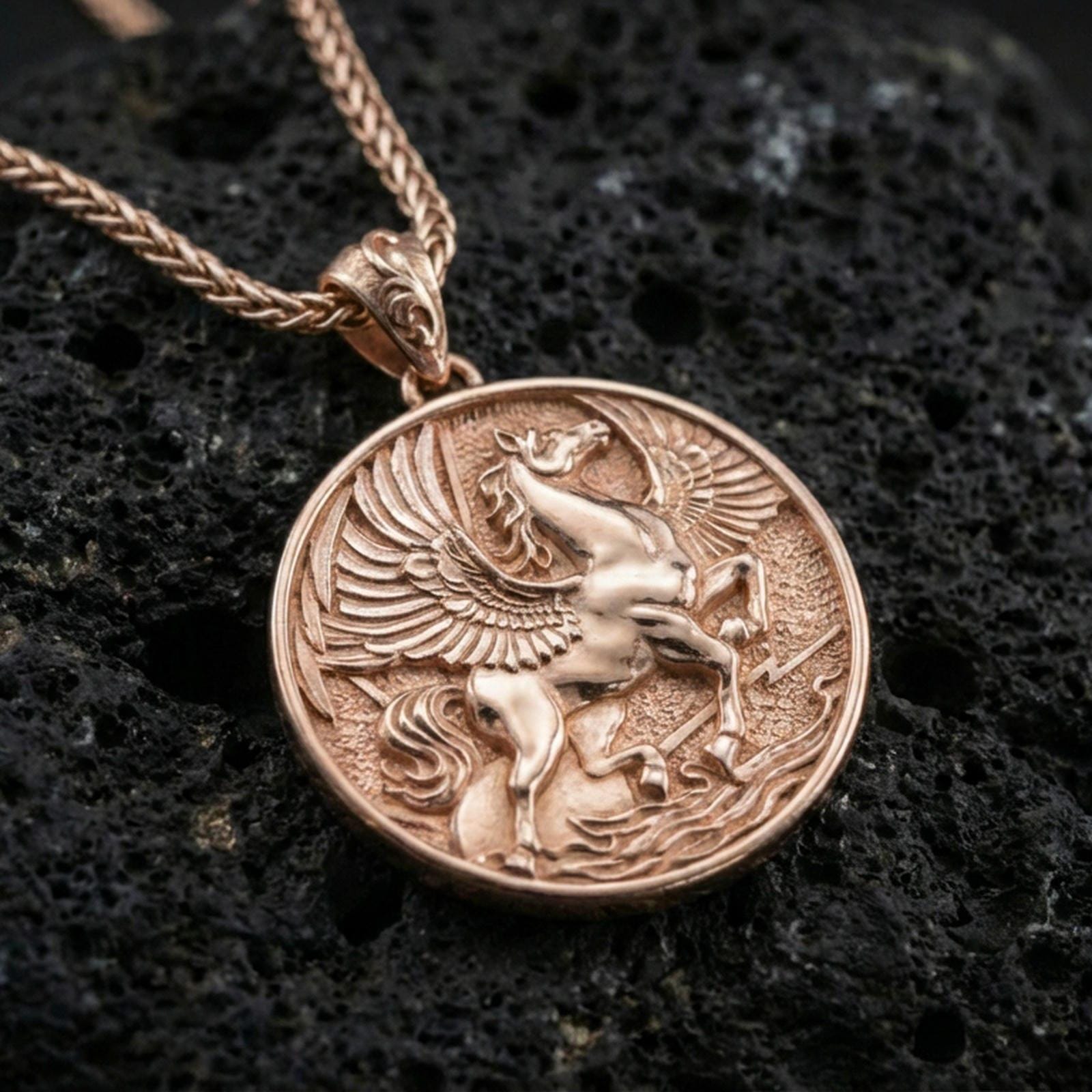 Rose gold plated winged Pegasus medallion pendant on volcanic rock, textured lava stone background, ornate relief detail
