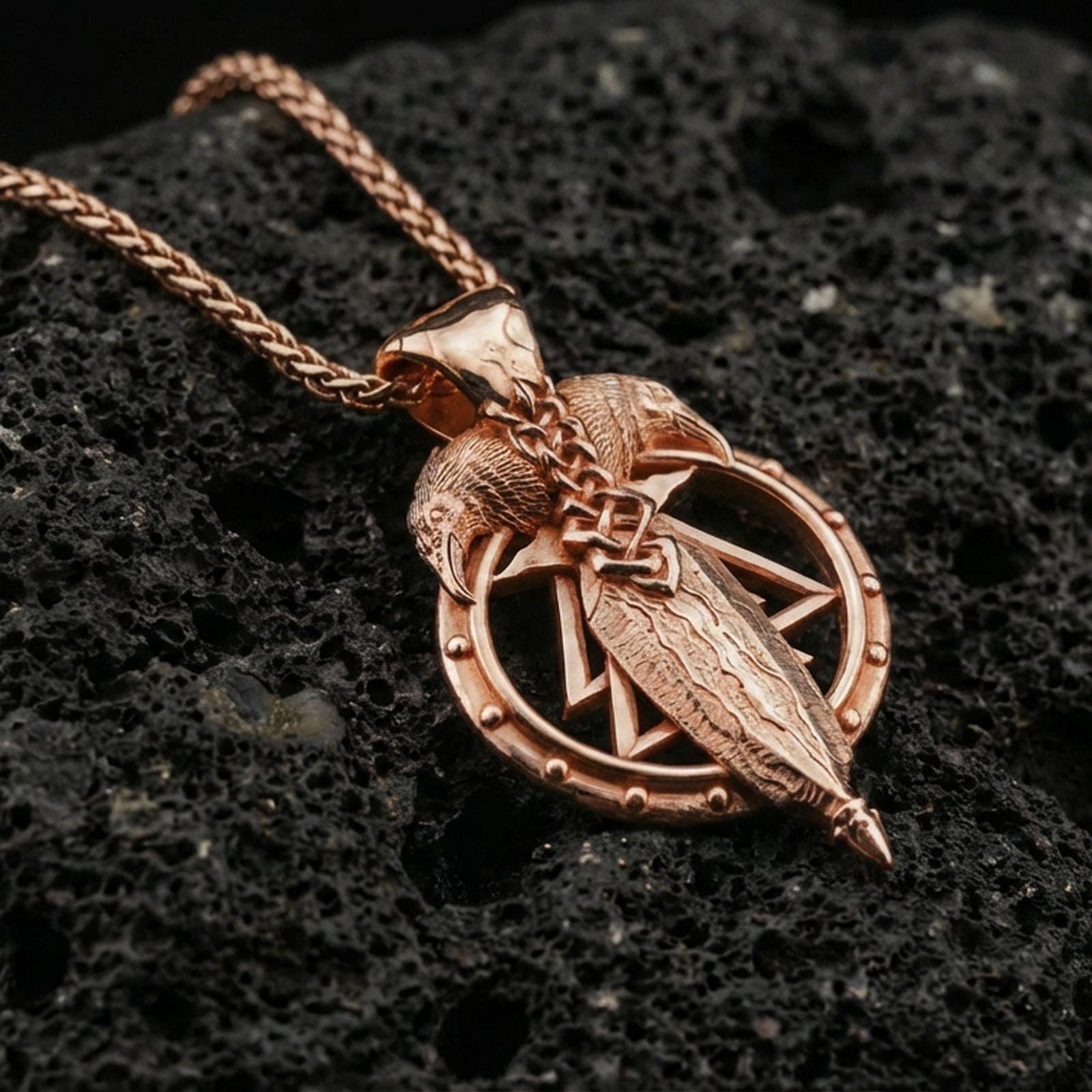 Rose gold plated raven and spear pendant on volcanic rock, textured lava stone background, high-relief metalwork detail