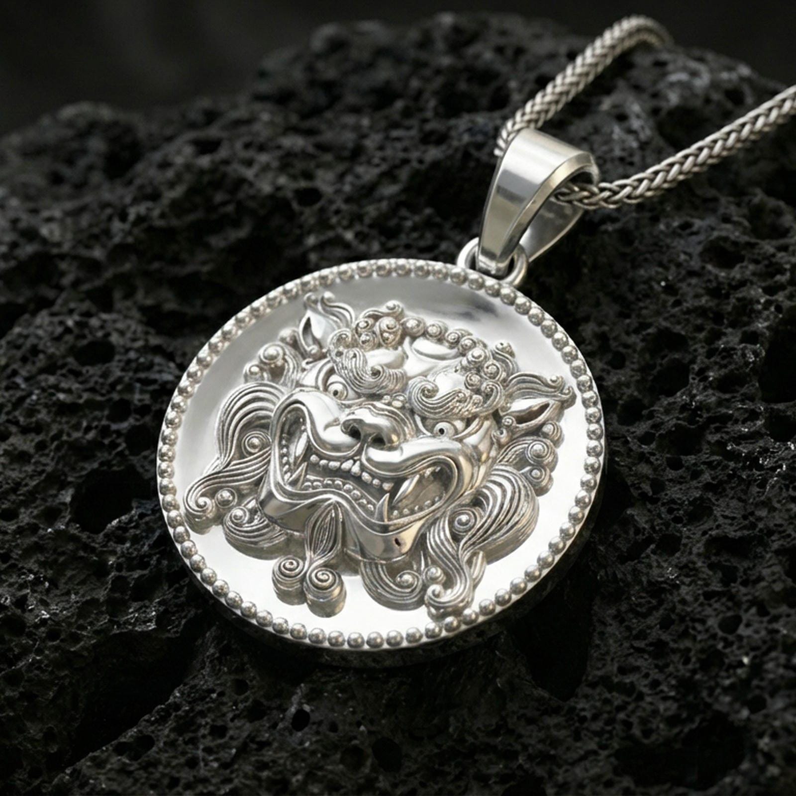 Polished silver guardian lion medallion necklace on volcanic rock, crisp sculpted face and textured background, close-up