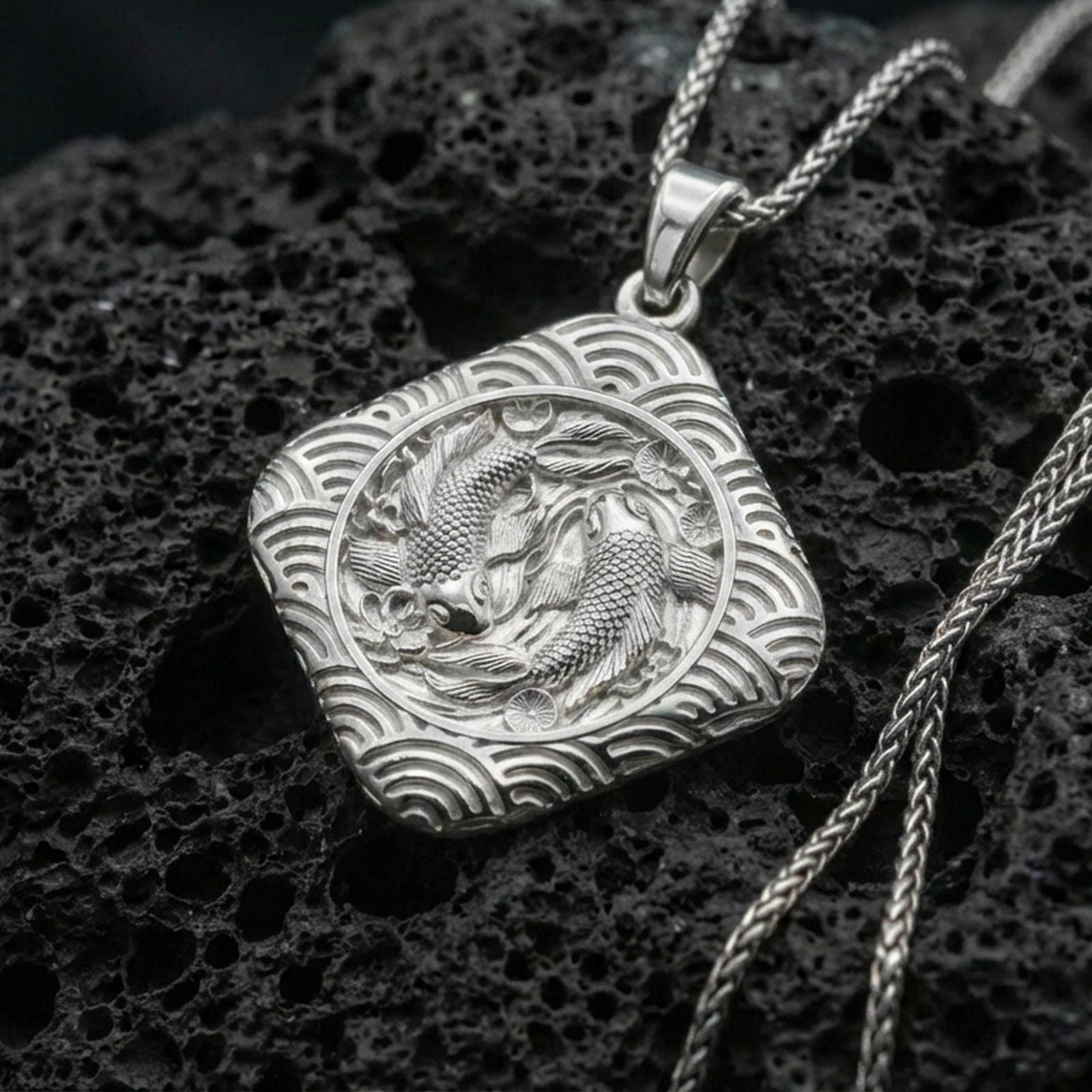 Polished silver koi fish necklace on volcanic rock, crisp scale texture and wave pattern border, close-up lighting