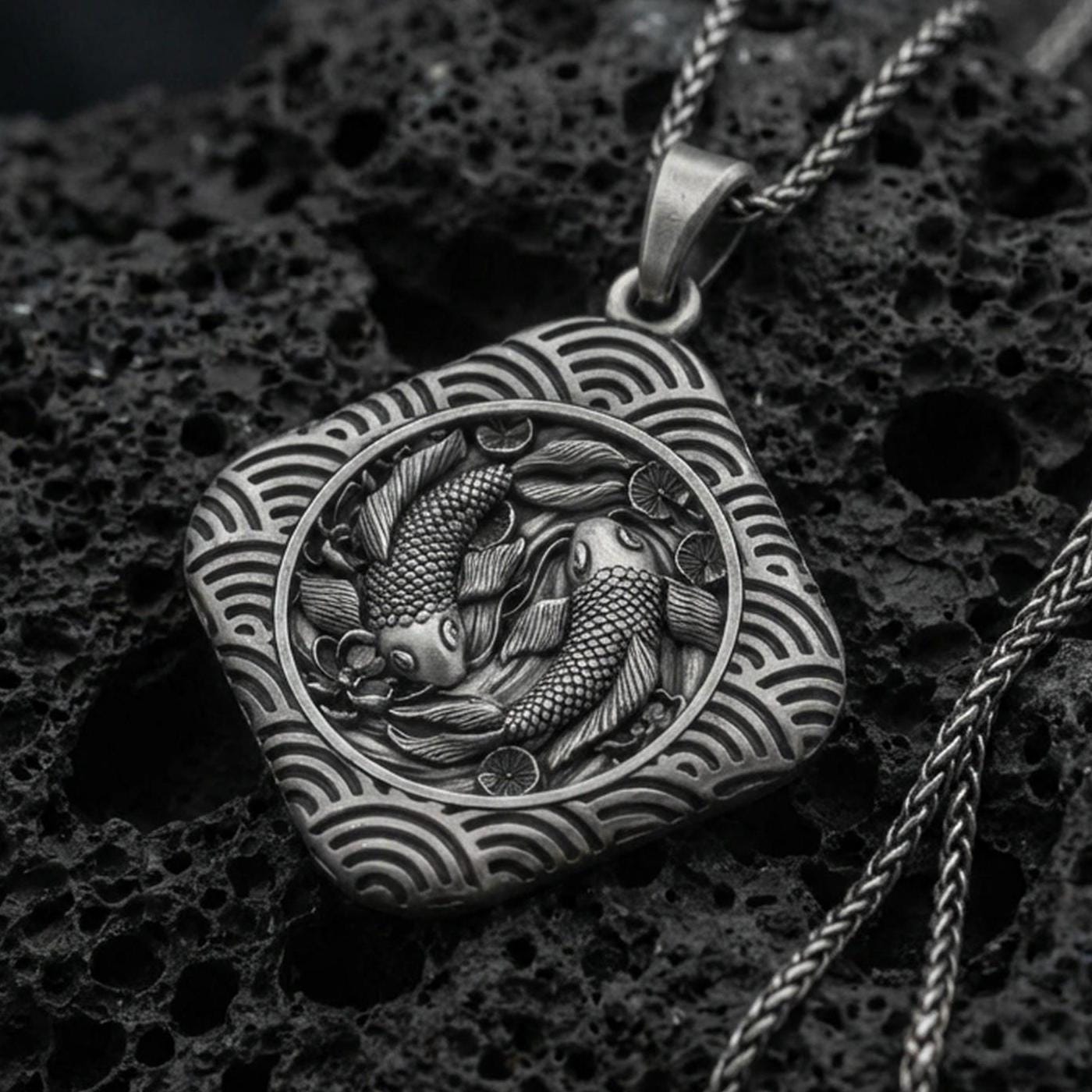 Oxidized sterling silver koi fish pendant on volcanic rock, twin koi relief in framed medallion, macro studio shot