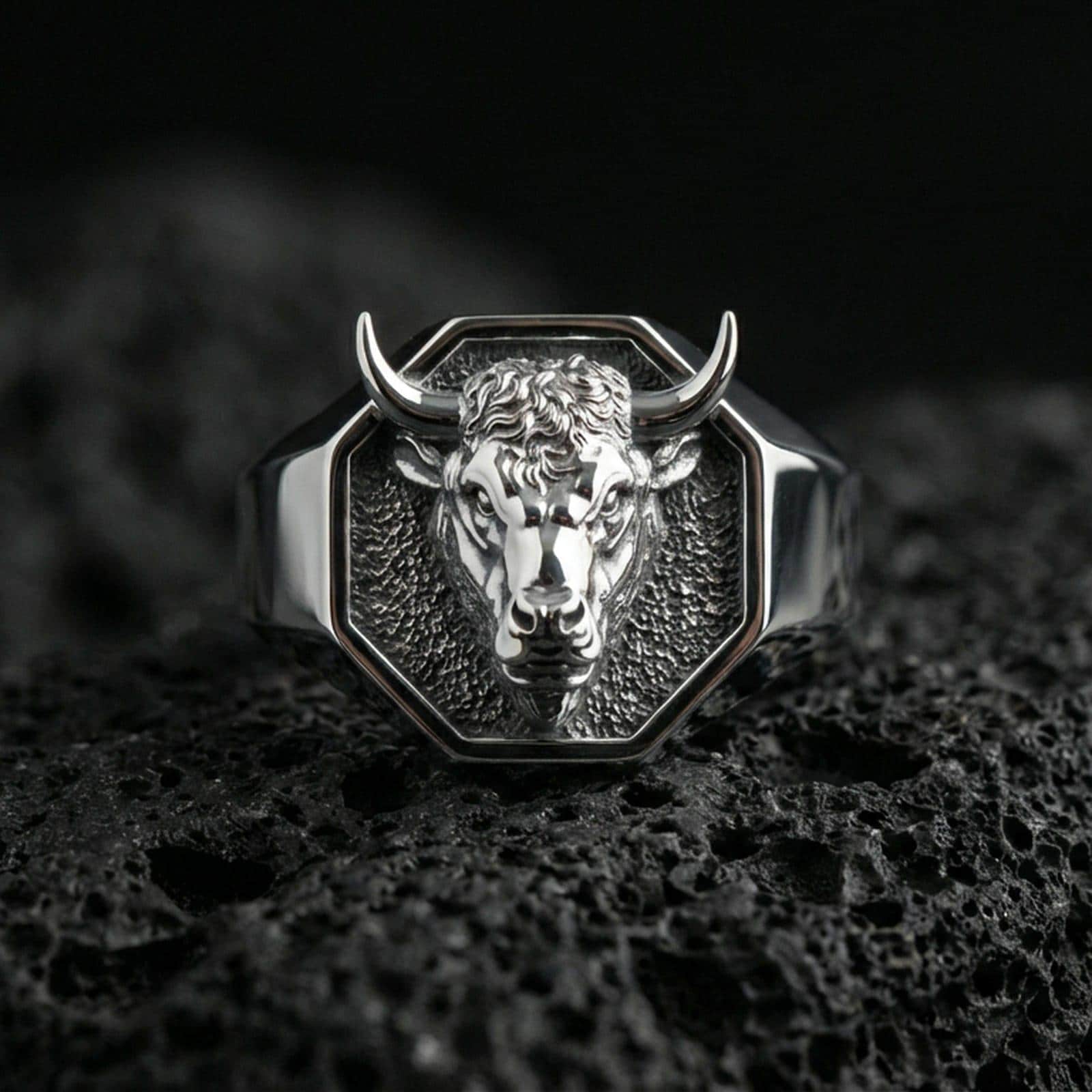 Polished silver bull head signet ring on volcanic rock, crisp sculpted muzzle and clean geometric bezel, close-up lighting