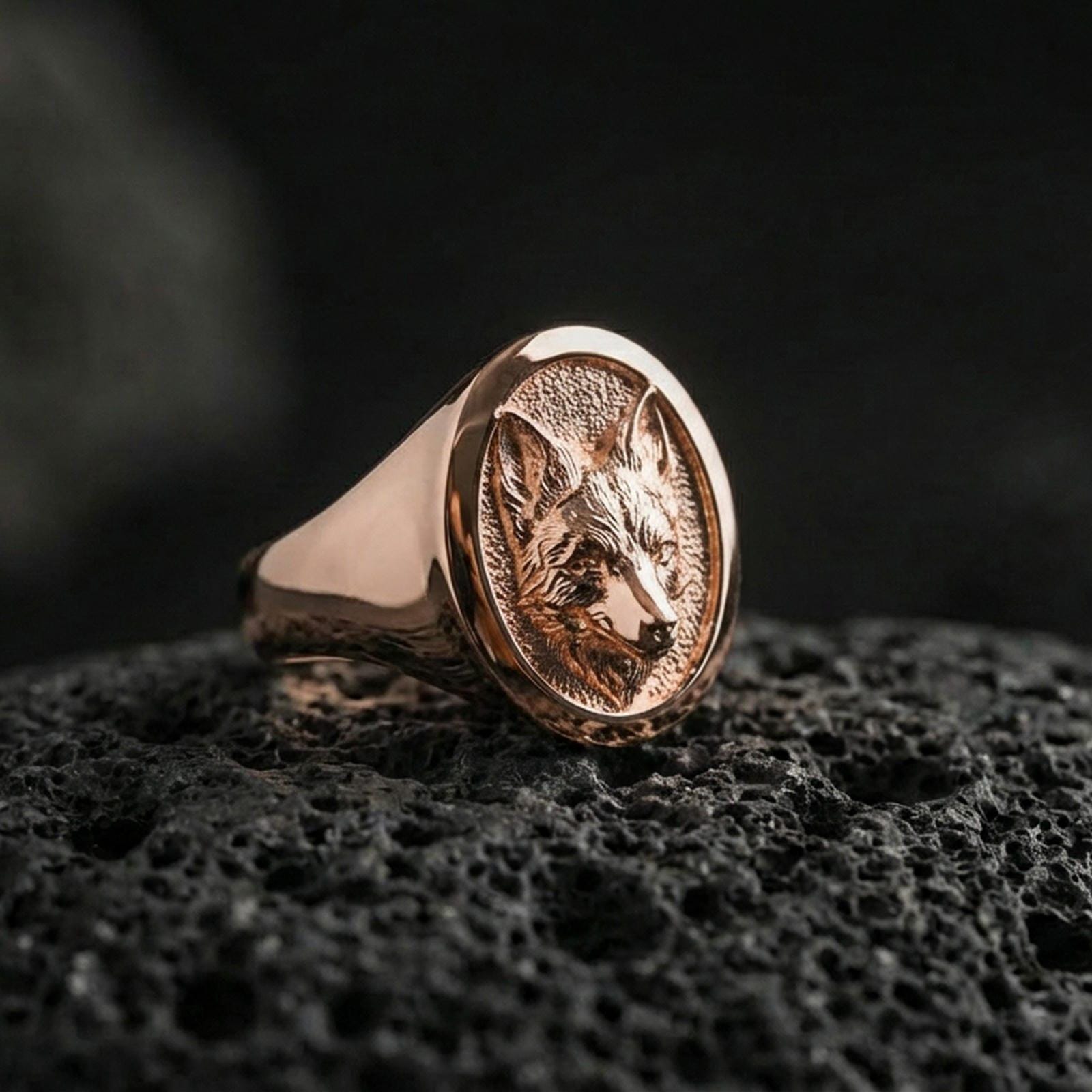 Rose gold plated fox head signet ring on volcanic rock, textured lava stone background, refined fox portrait engraving
