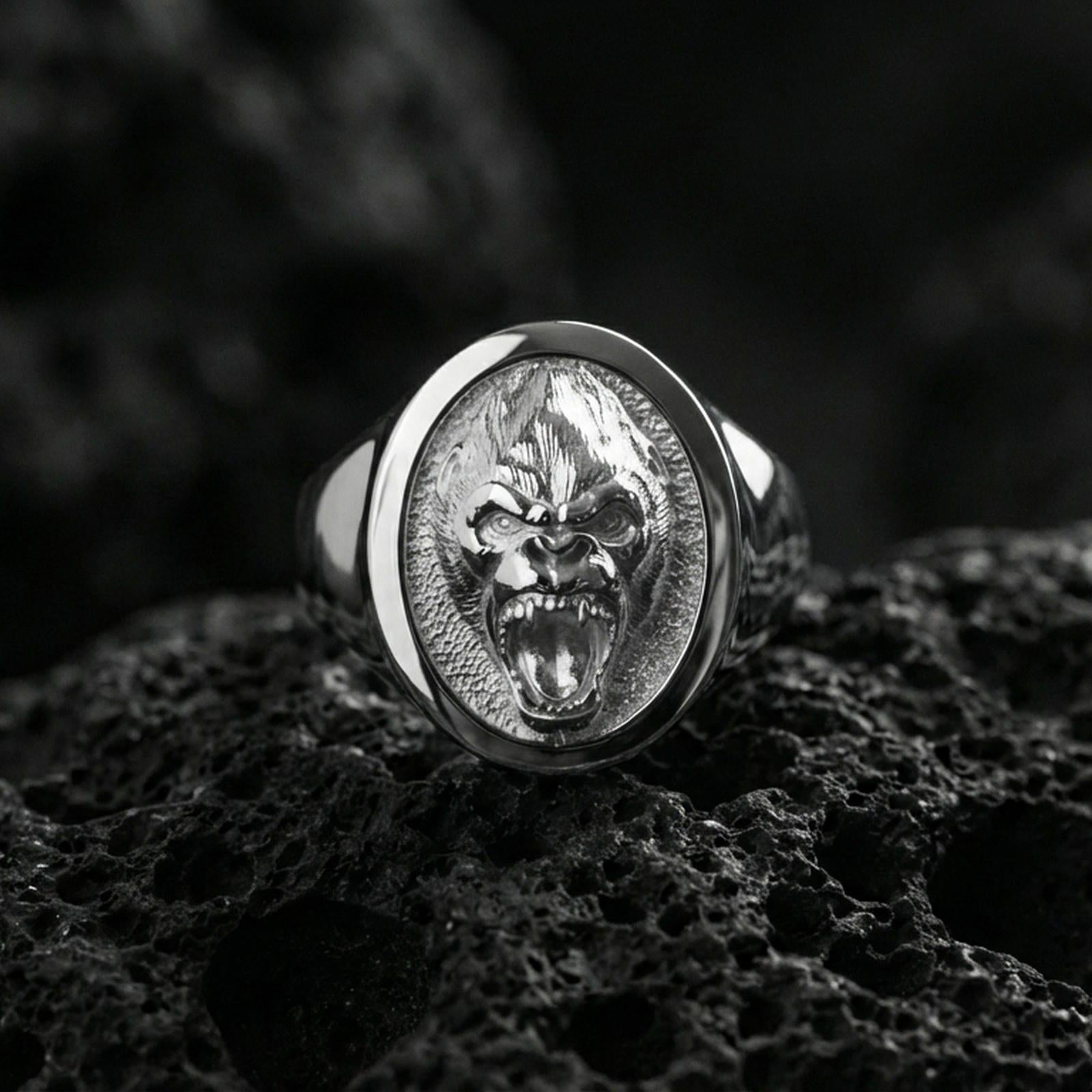 Polished silver gorilla head signet ring on volcanic rock, crisp facial contours and textured background, close-up lighting