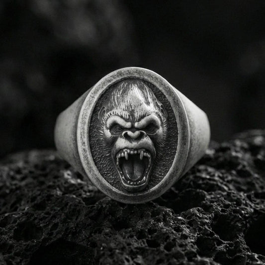 Oxidized sterling silver gorilla head signet ring on volcanic rock, roaring face relief with sharp fangs, macro studio shot