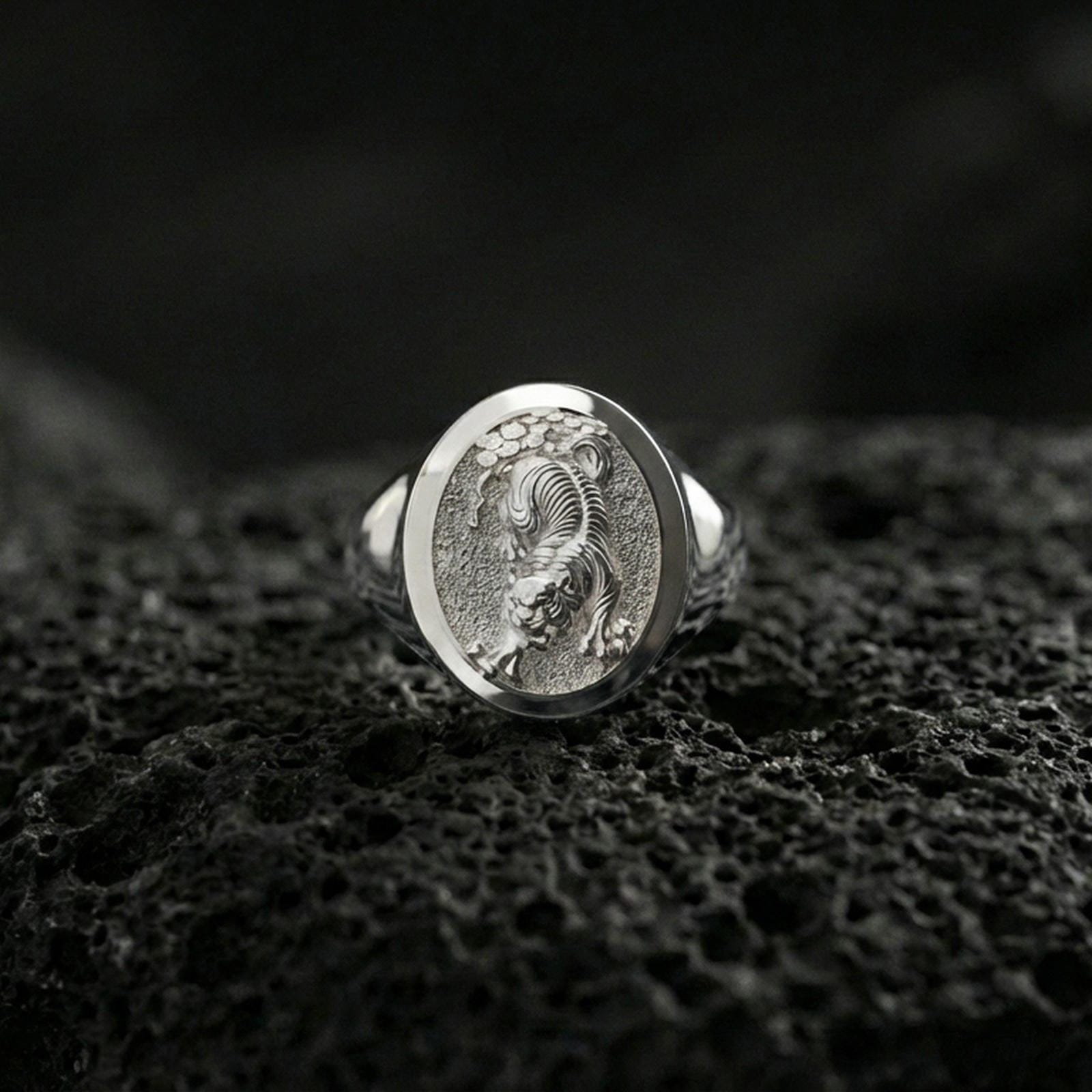 Polished silver tiger signet ring on volcanic rock, crisp stripe carving and clean oval bezel edge, close-up lighting
