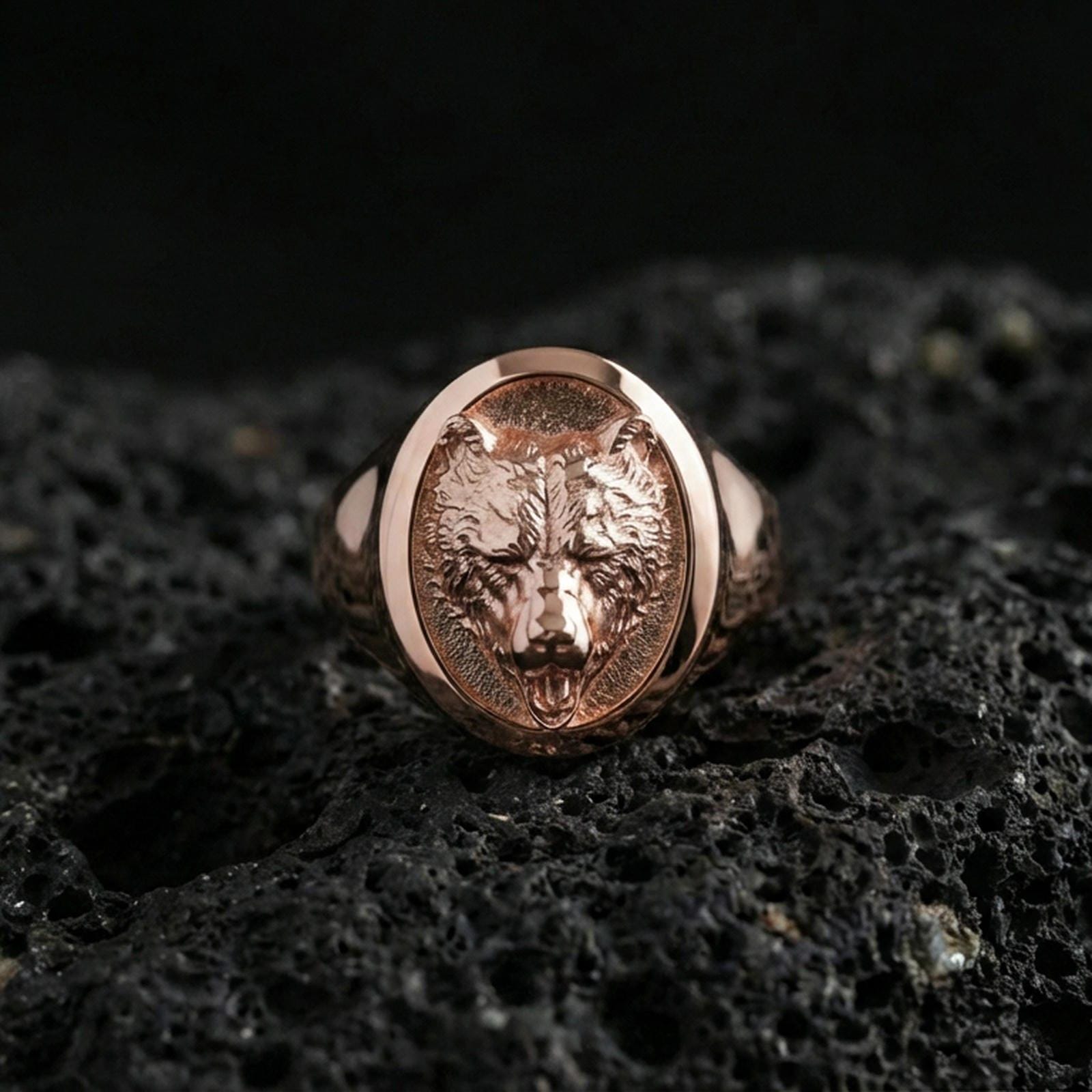 Rose gold plated bear signet ring on volcanic rock, textured lava stone background, detailed bear face engraving and depth
