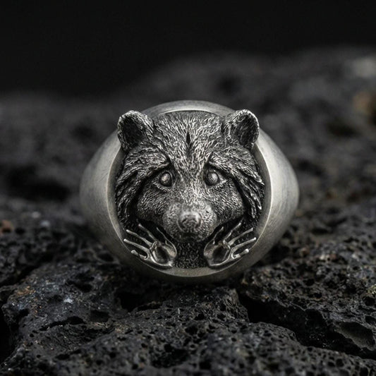 Oxidized sterling silver raccoon head signet ring on volcanic rock, detailed fur texture and paws relief, macro studio shot