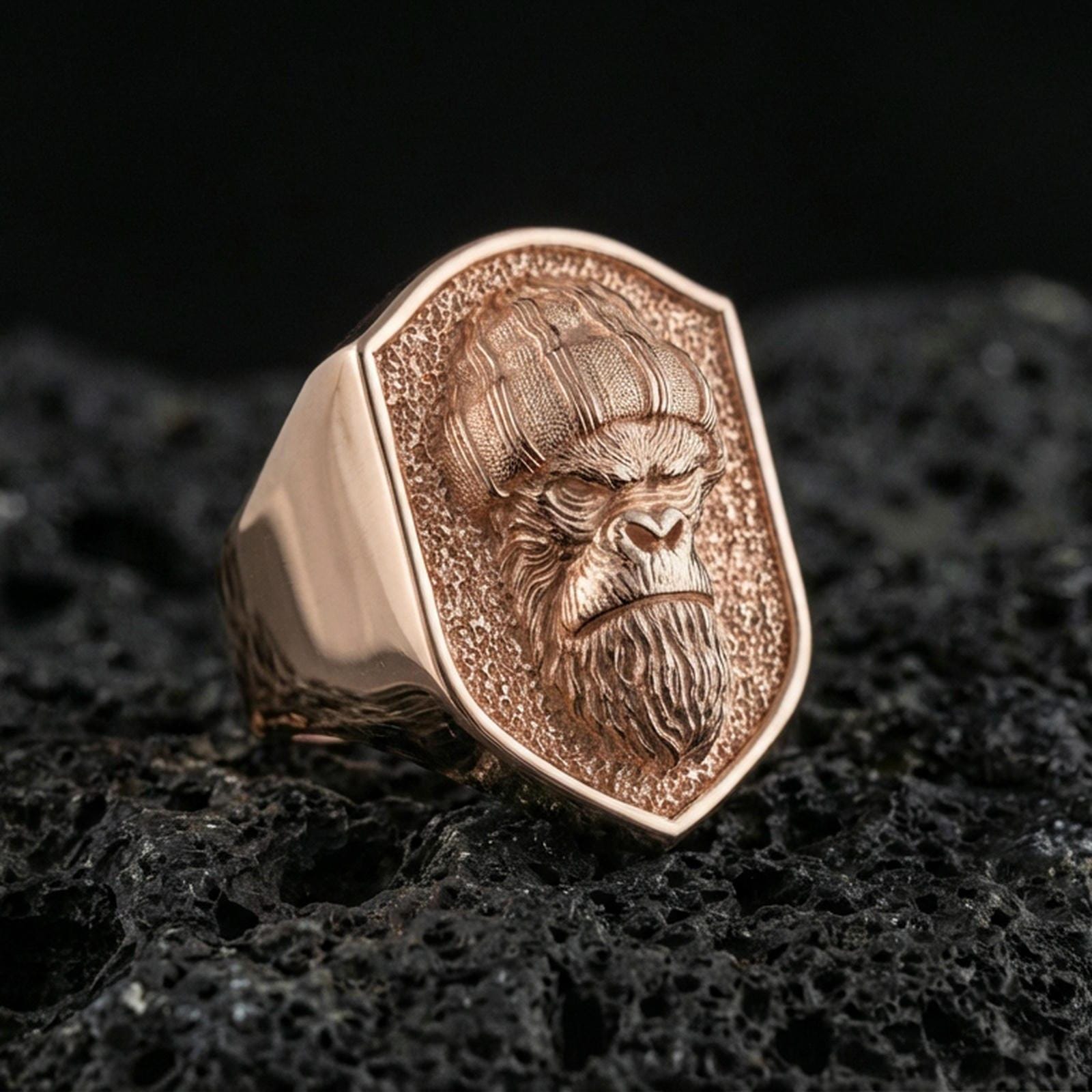 Rose gold plated gorilla warrior signet ring on volcanic rock, textured lava stone background, detailed helmet and fur engraving