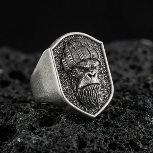 Oxidized sterling silver gorilla warrior signet ring on volcanic rock, shield-shaped face with textured background, macro studio shot
