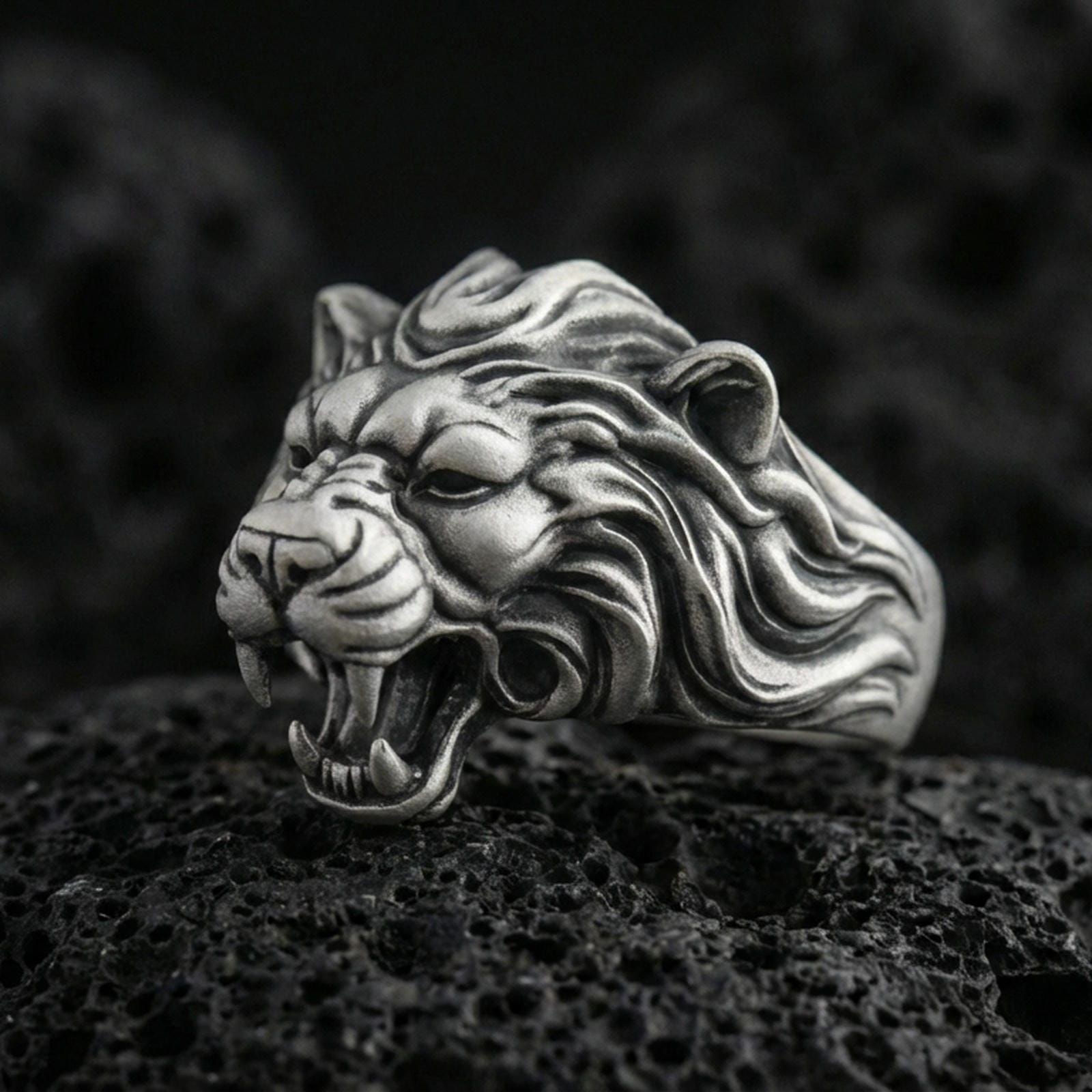 Oxidized sterling silver angry lion king ring on volcanic rock, roaring lion head with sculpted mane, macro studio close-up