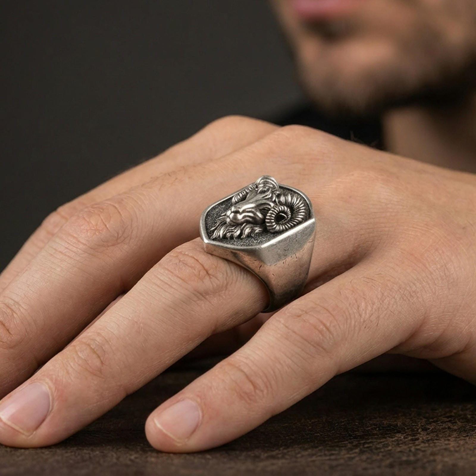 Oxidized ram head signet ring worn on finger, lifestyle close-up, masculine statement ring with raised horn design