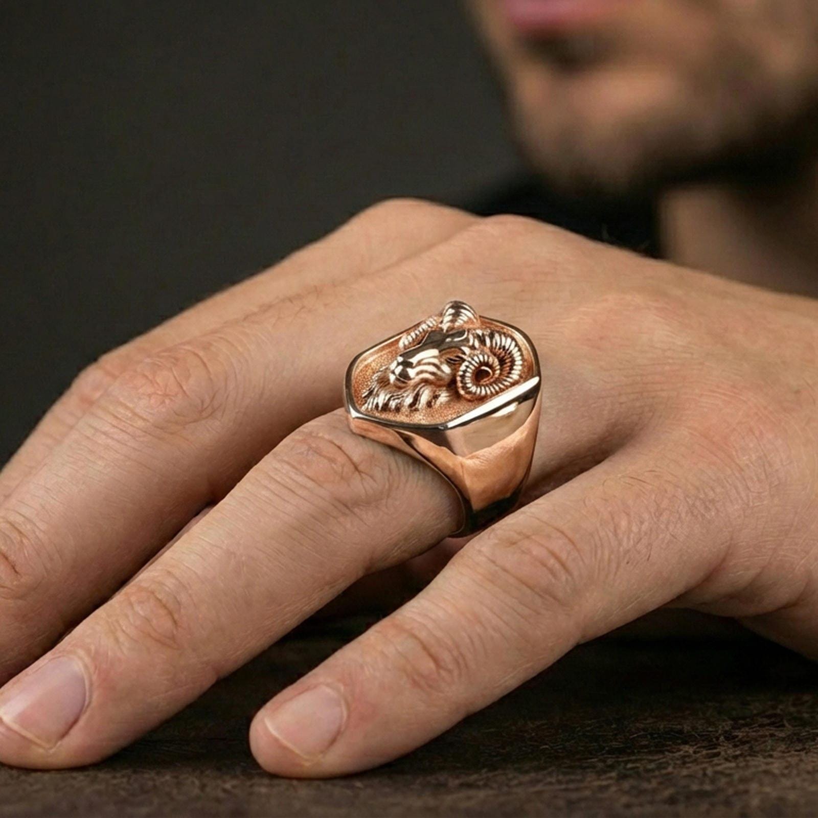 Rose gold plated ram head signet ring worn on finger, lifestyle wear photo, warm tone highlighting ram horns and relief