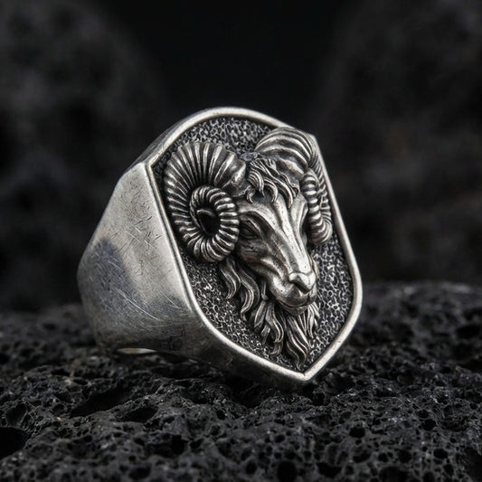 Oxidized sterling silver ram head signet ring on volcanic rock, curved horn relief and textured background, macro product shot