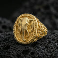 Load image into Gallery viewer, Gold plated elephant signet ring on volcanic rock, bold elephant portrait with decorative border and carved side patterns, premium macro lighting
