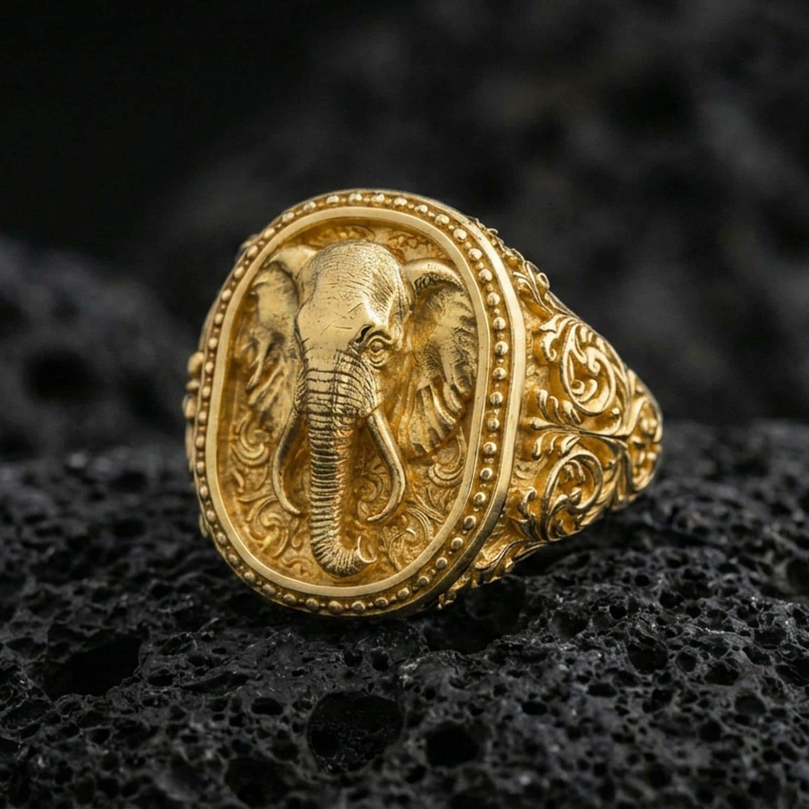 Gold plated elephant signet ring on volcanic rock, bold elephant portrait with decorative border and carved side patterns, premium macro lighting