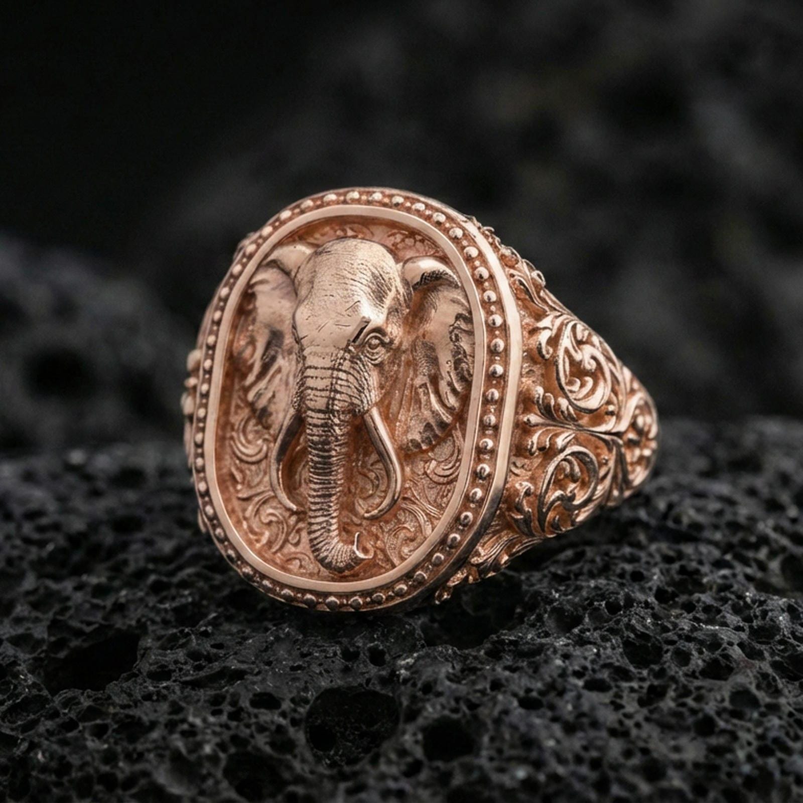 Rose gold plated elephant signet ring on volcanic rock, elephant head signet ring with textured relief and ornate swirl band, luxury close-up