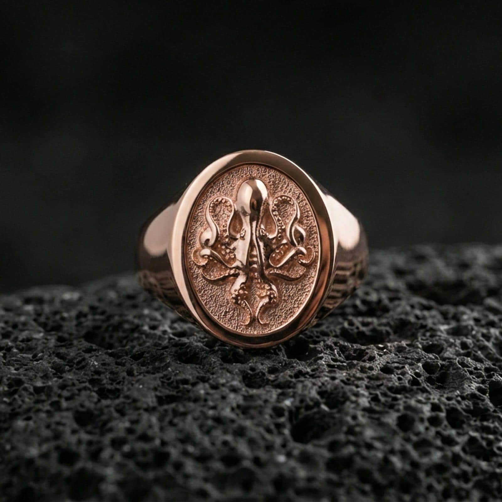 Rose gold plated octopus signet ring on volcanic rock, sculpted octopus crest signet ring with high-relief tentacle details, luxury close-up