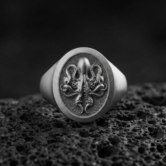 Oxidized sterling silver octopus signet ring on volcanic rock, raised octopus emblem on round face with textured background, macro product photo