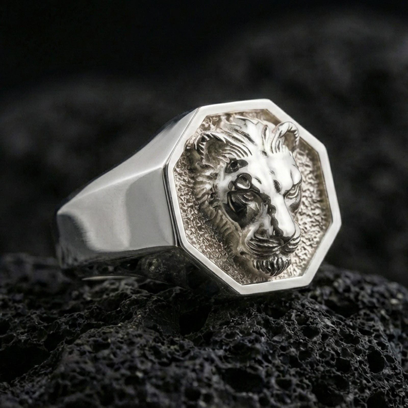 Polished silver lioness signet ring on volcanic rock, octagonal bezel with sculpted lioness portrait and crisp edge lines, close-up jewelry shot
