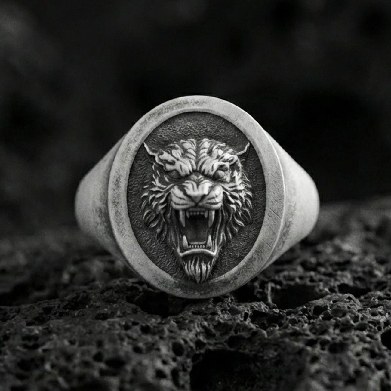 Oxidized sterling silver tiger signet ring on volcanic rock, oval face with roaring tiger head relief and dark textured background, macro product photo
