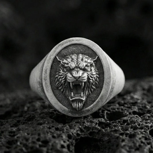 Oxidized sterling silver tiger signet ring on volcanic rock, oval face with roaring tiger head relief and dark textured background, macro product photo