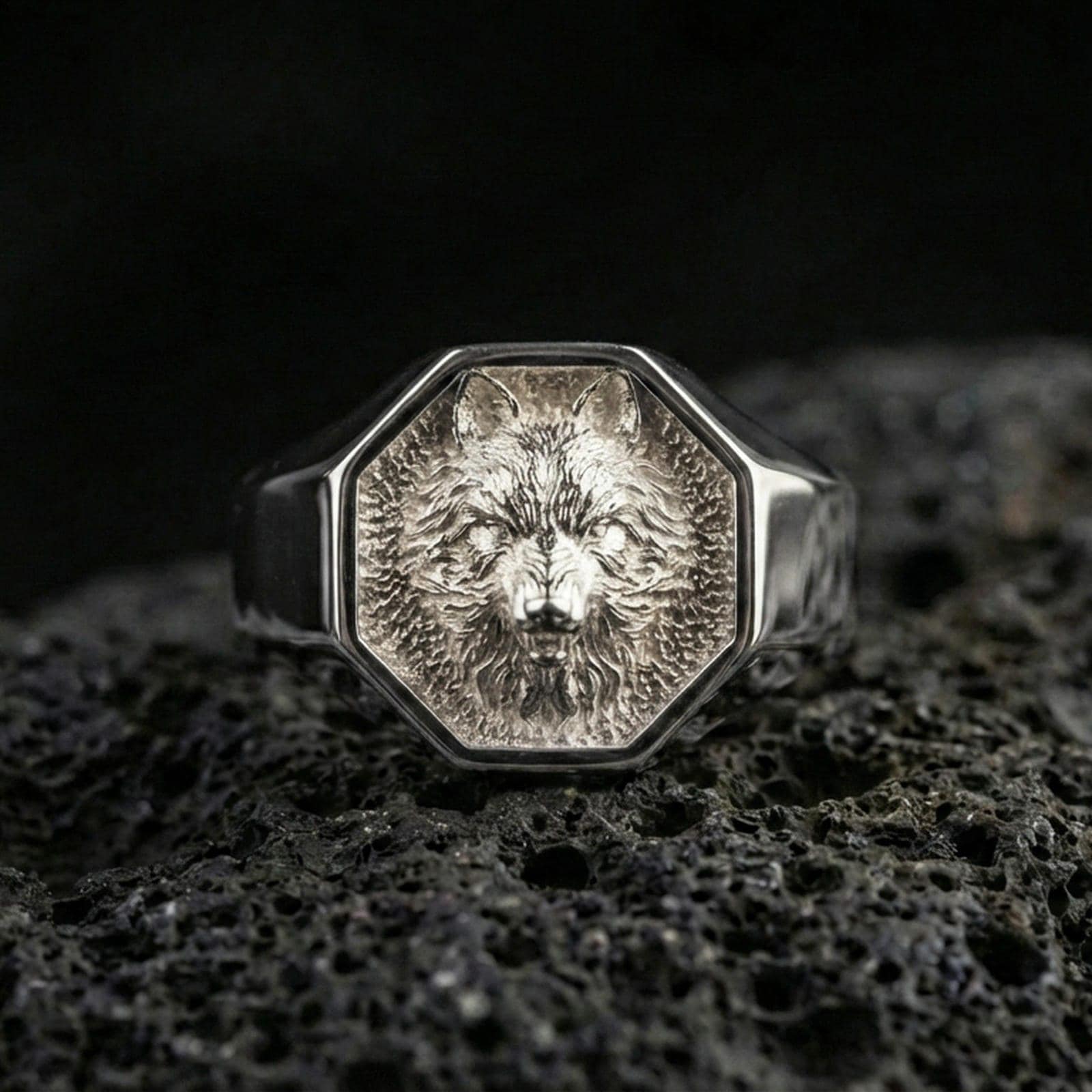 Polished silver wolf signet ring on volcanic rock, octagon bezel with detailed wolf portrait and clean sharp edges, close-up jewelry shot