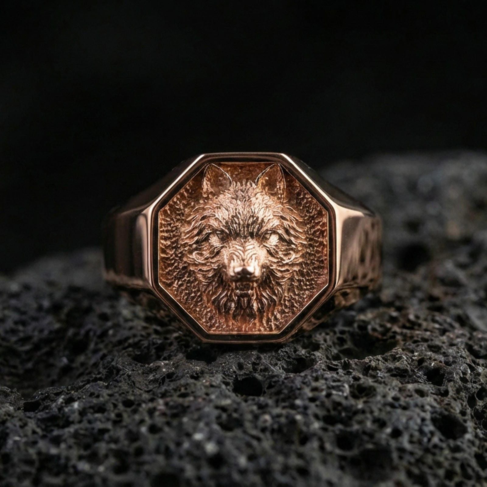 Rose gold plated wolf signet ring on volcanic rock, octagon wolf head emblem ring with defined muzzle and layered fur details, luxury macro