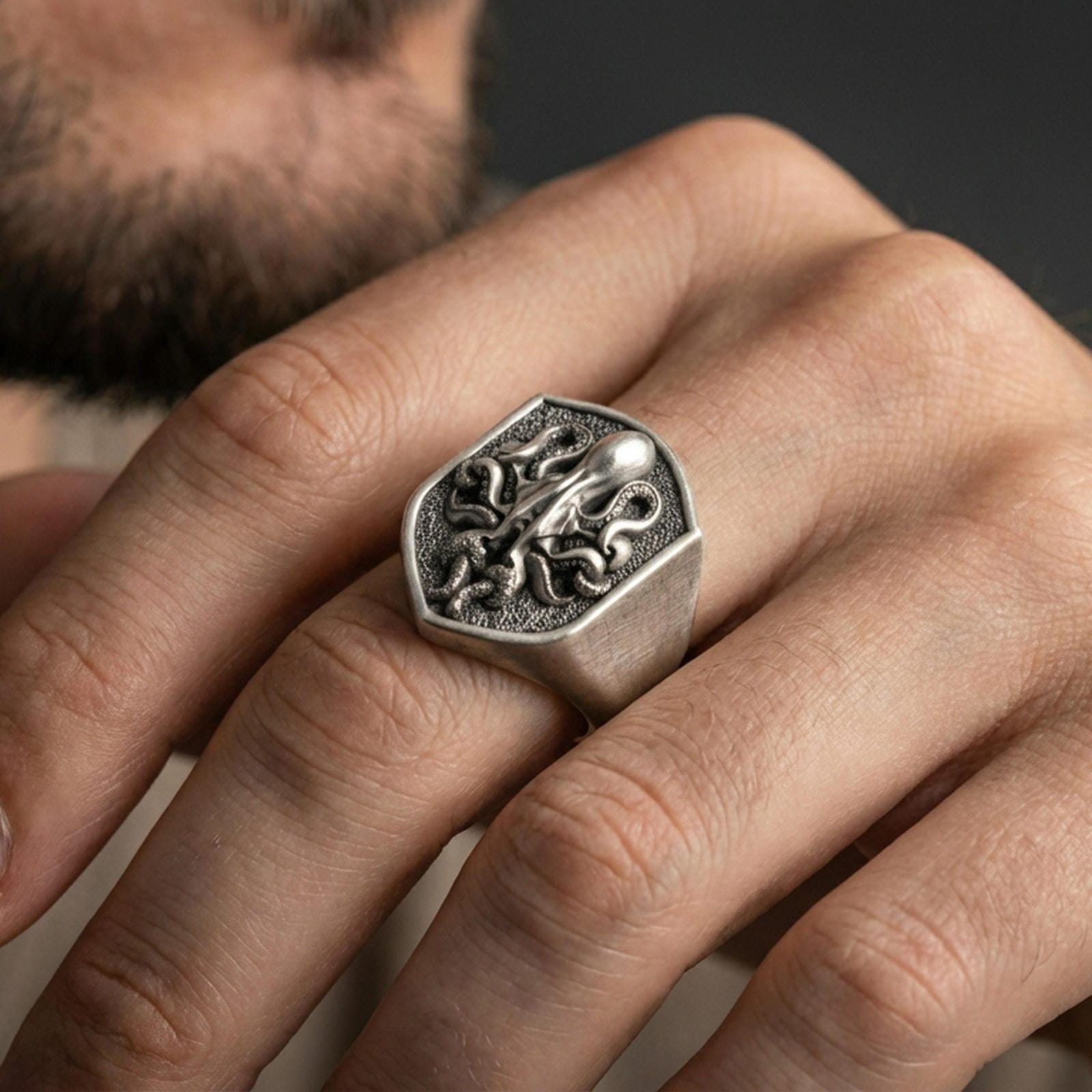 Oxidized shield octopus signet ring worn on finger, lifestyle close-up showing raised sea creature emblem on wide tapered band