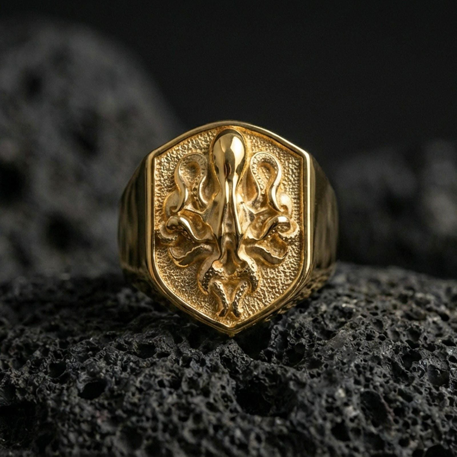 Gold plated octopus signet ring on volcanic rock, shield-shaped nautical emblem with detailed tentacle texture and deep contrast field, studio macro lighting