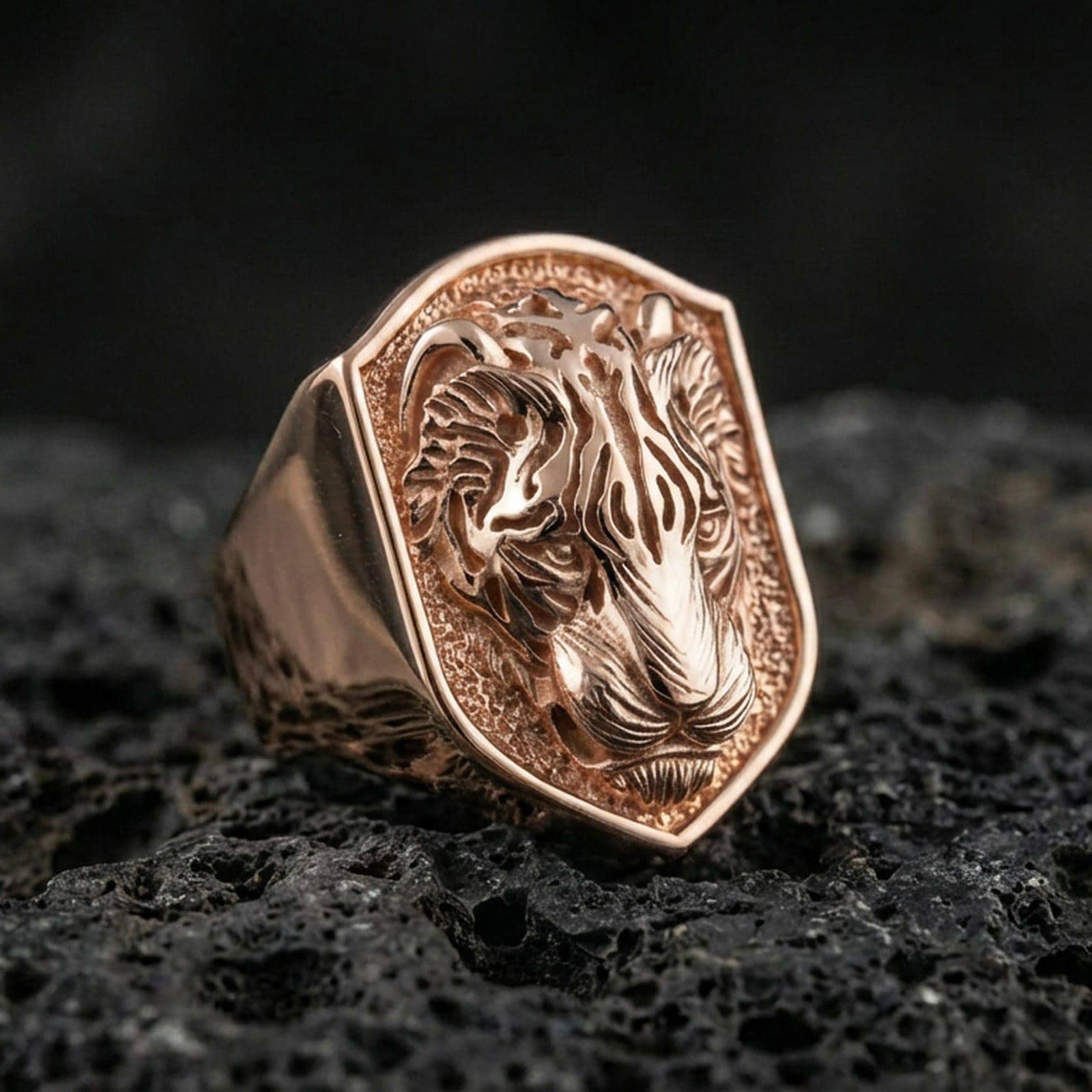 Rose gold plated tiger signet ring on volcanic rock, shield tiger crest signet with engraved stripe details and rugged recessed background, luxury product photo