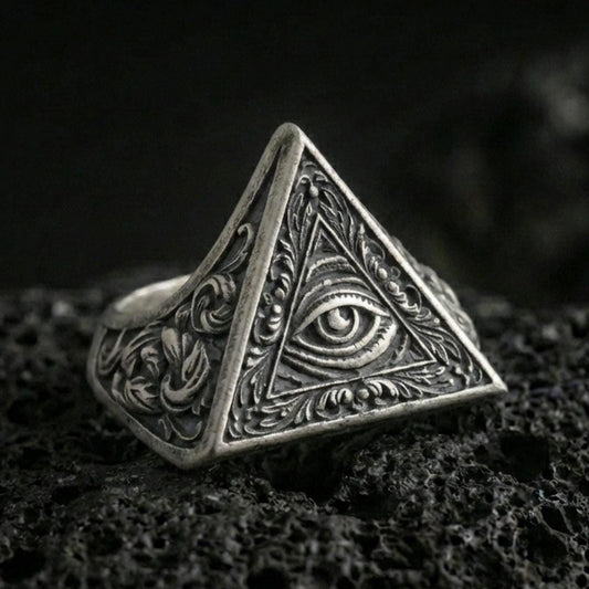 Oxidized sterling silver triangle signet ring with all-seeing eye relief and ornate scroll engravings, macro shot on black volcanic rock