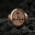 Load image into Gallery viewer, Rose gold plated oval signet ring with occult sigil engraving and textured signet surface, close-up on volcanic rock
