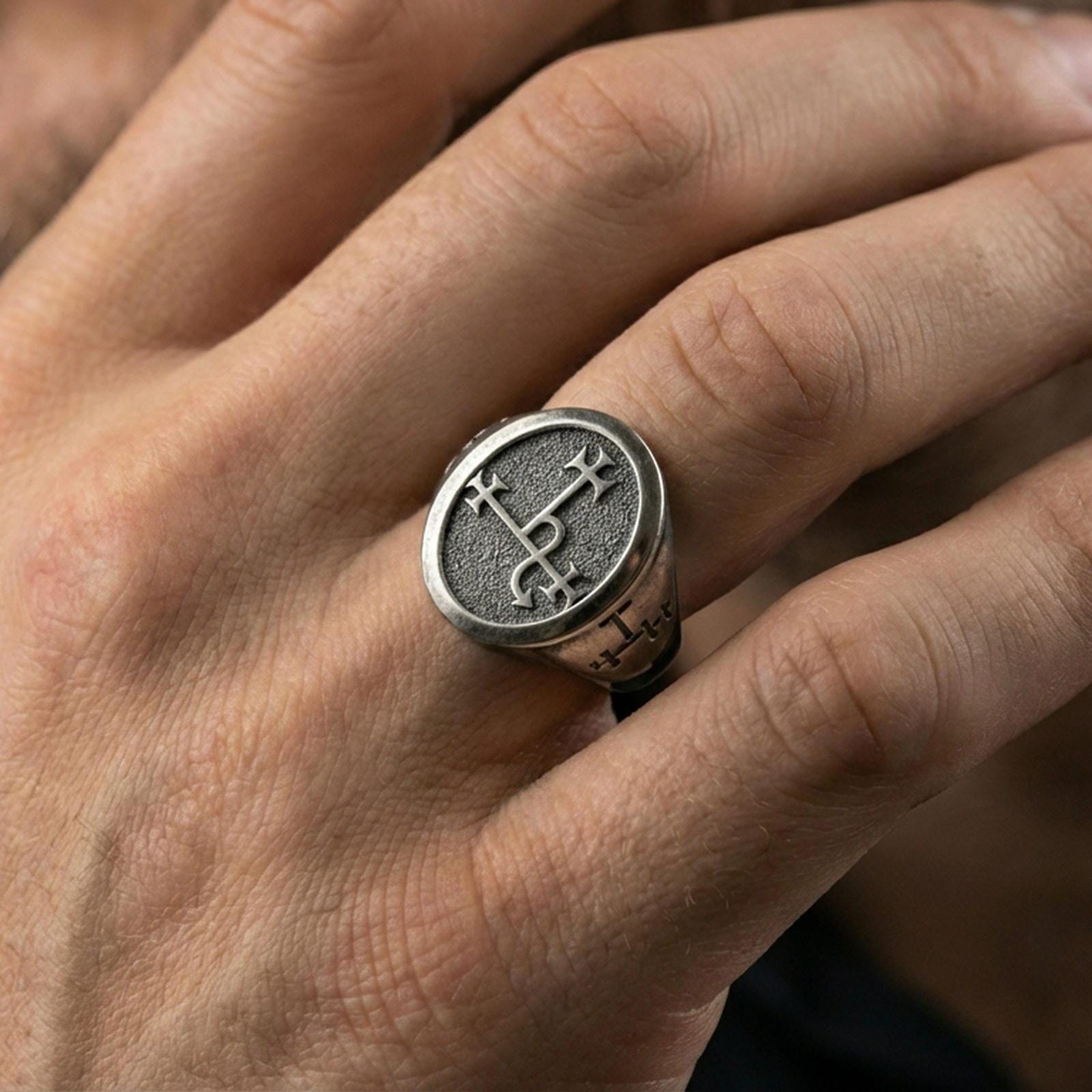 Oxidized oval signet ring worn on a finger, close-up lifestyle photo highlighting the engraved sigil and solid band profile