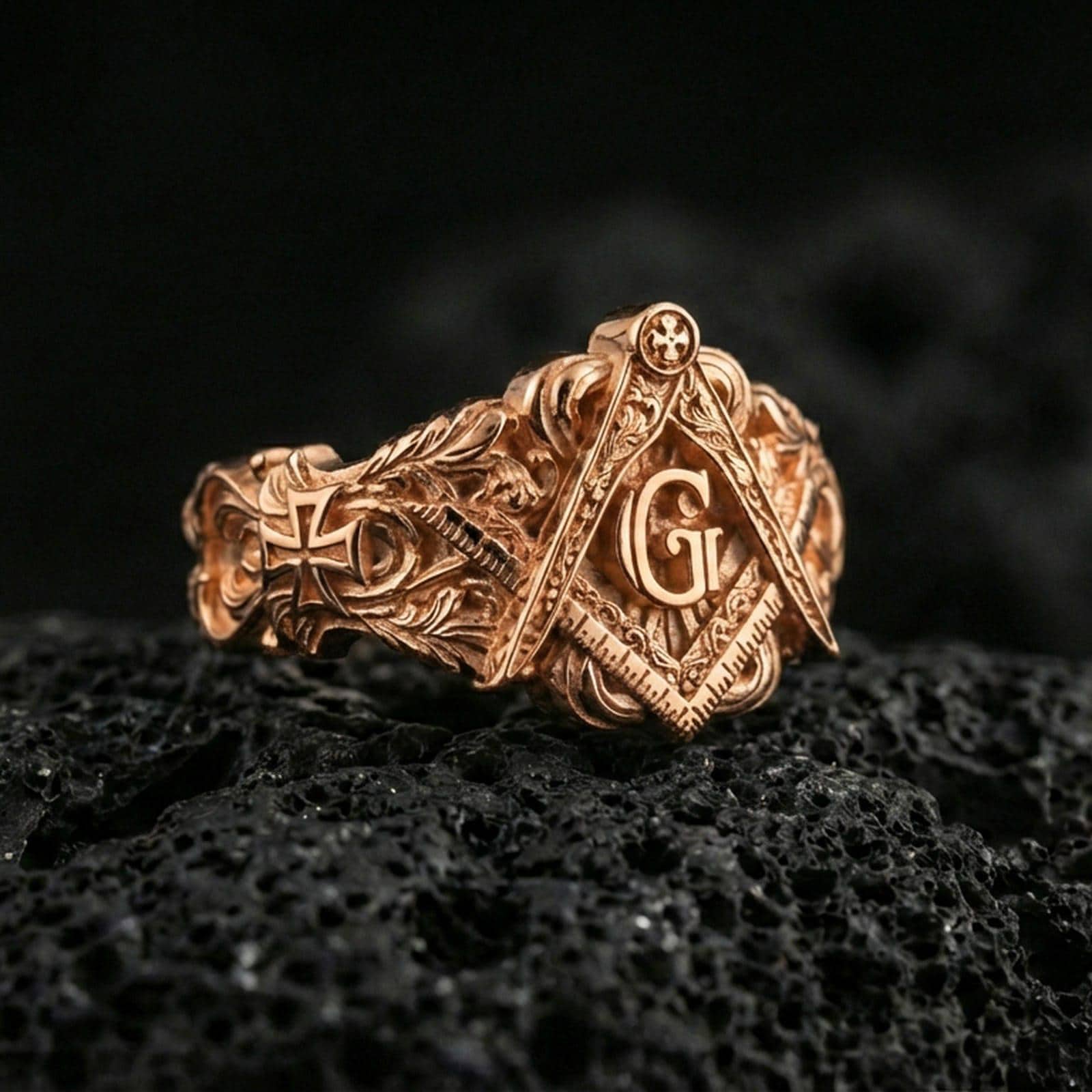 Rose gold plated Freemason square and compass ring with “G” emblem and carved ornamental band, macro shot on volcanic rock