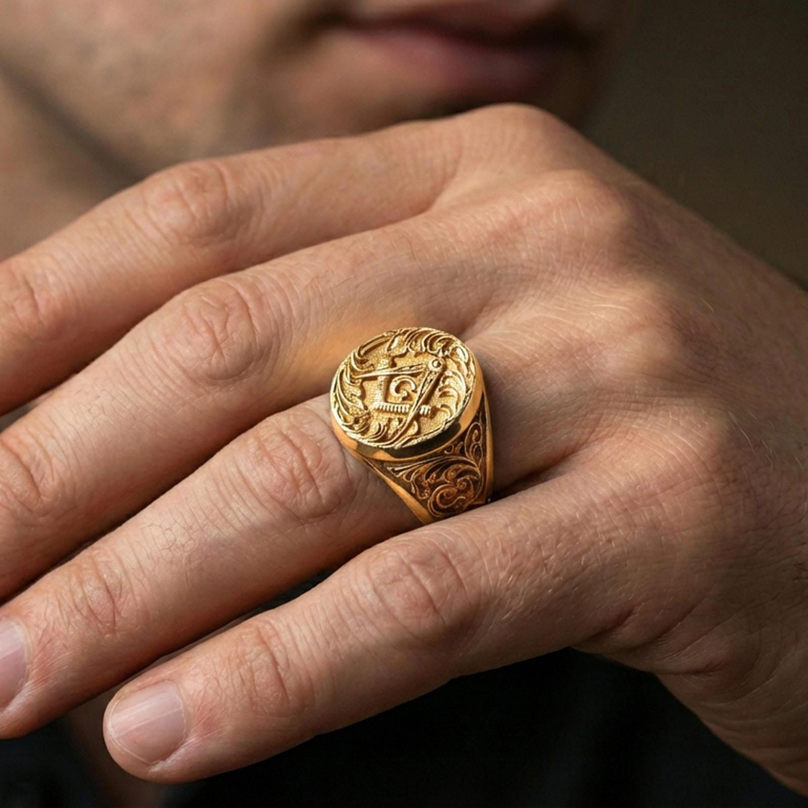 Gold plated square and compass Masonic ring worn on a finger, lifestyle macro emphasizing the engraved signet face