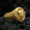Load image into Gallery viewer, Gold plated Japanese oni mask signet ring with seigaiha wave engraved band and ornate frame around the horned demon face, macro on volcanic rock
