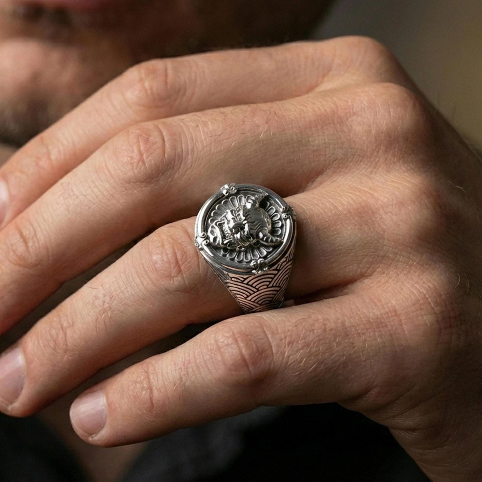 Polished silver Japanese oni signet ring on the finger with seigaiha wave band engraving, wearable macro emphasizing the framed demon face