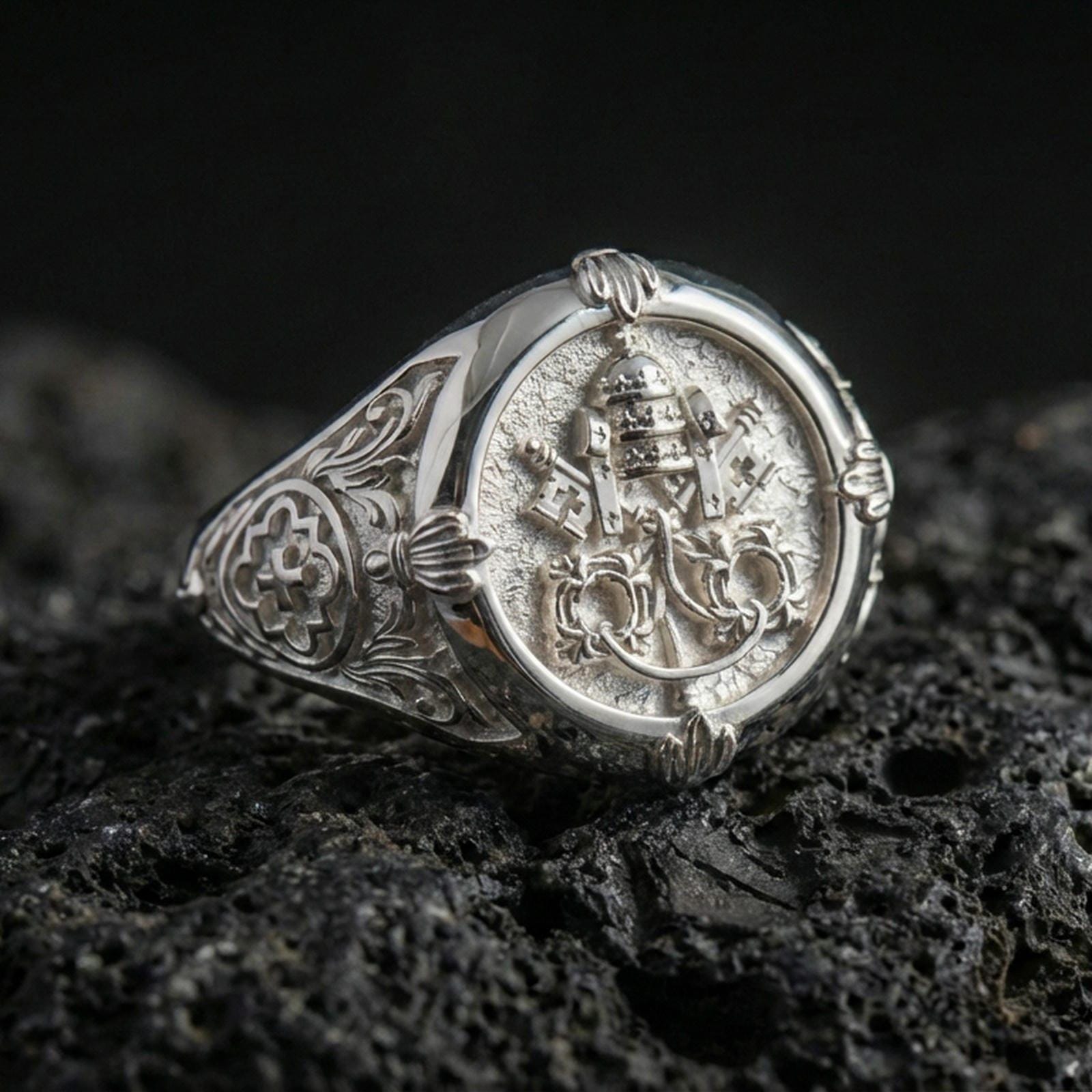 Polished silver Saint Peter Keys of Heaven signet ring with detailed Vatican key emblem and ornate sides, close-up on volcanic stone