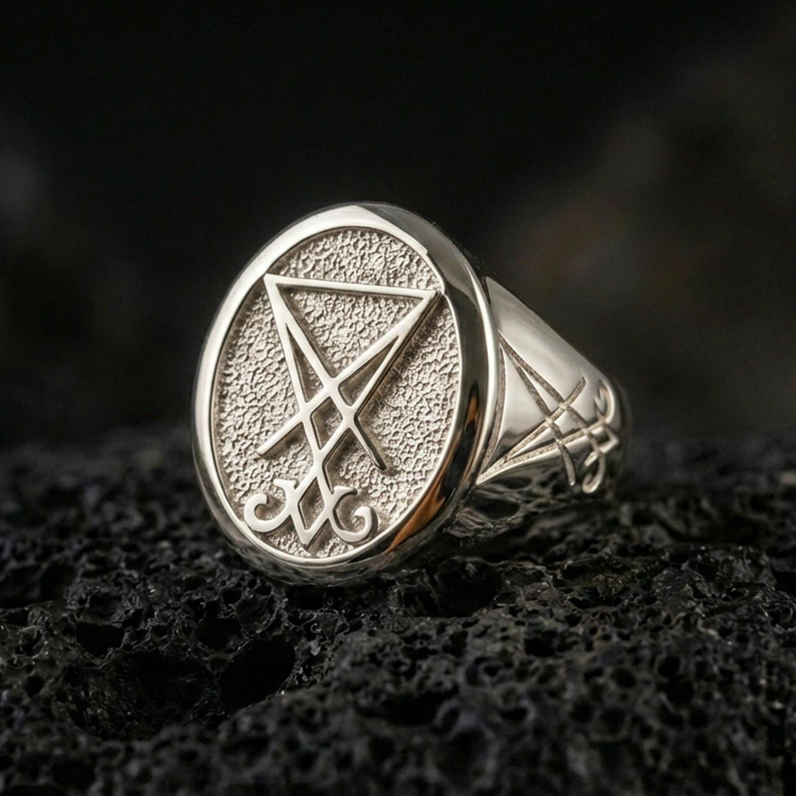 Polished silver Lucifer sigil signet ring featuring a bold raised emblem and clean beveled edges, close-up on volcanic stone