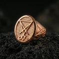 Load image into Gallery viewer, Rose gold plated Lucifer sigil signet ring with raised sigil emblem and matte-textured face, close-up on volcanic rock
