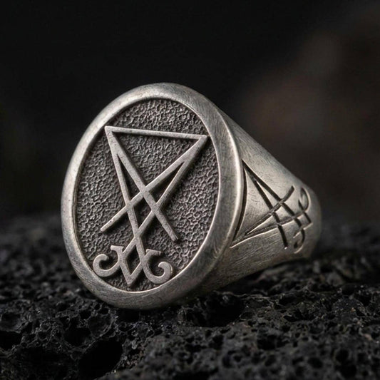 Oxidized sterling silver Lucifer sigil signet ring with raised occult symbol on a textured face, macro on black volcanic rock