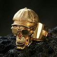 Load image into Gallery viewer, Sterling silver skull ring with a gold plated finish, cap-and-glasses skull design with deep shadowed engraving, macro on volcanic rock
