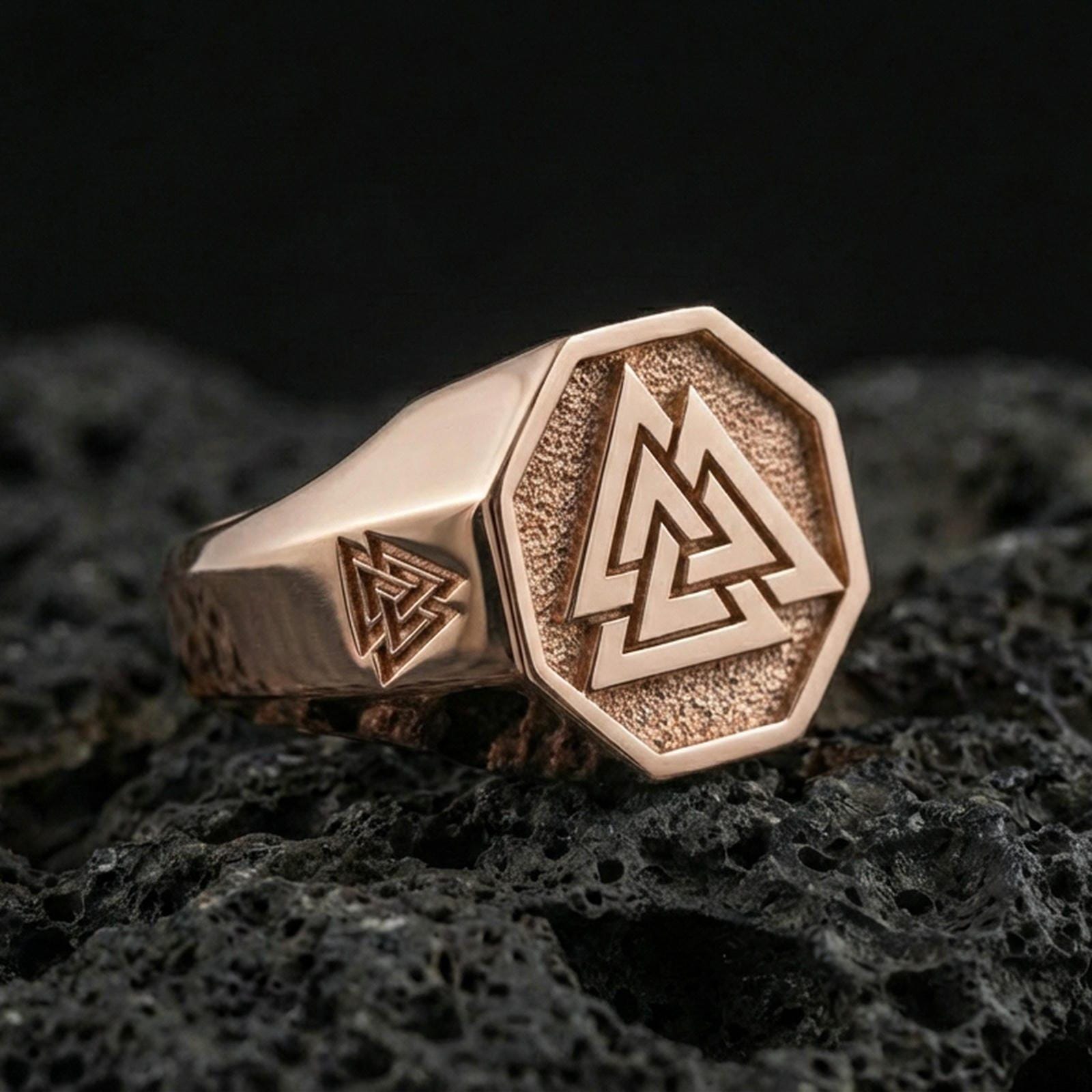 Sterling silver Valknut signet ring with a rose gold plated finish, octagonal signet face with the Norse Valknut symbol and side engraving, close-up on volcanic rock