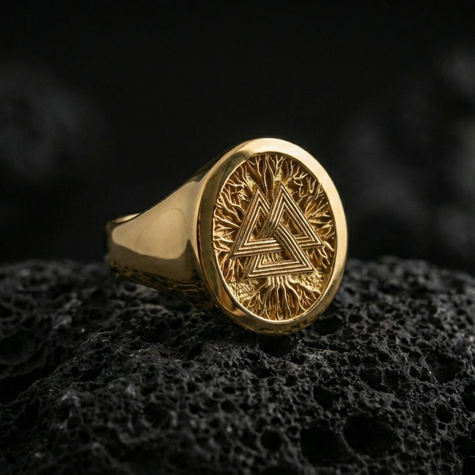 Sterling silver Valknut signet ring with a gold plated finish, round signet face showing the Valknut Norse symbol with textured background, macro on volcanic rock