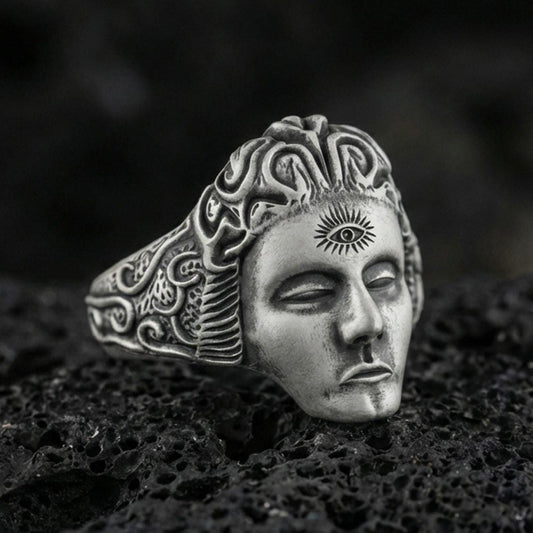 Sterling silver third eye face ring with an oxidized finish, sculpted calm mask and engraved swirling band details, macro on black volcanic rock
