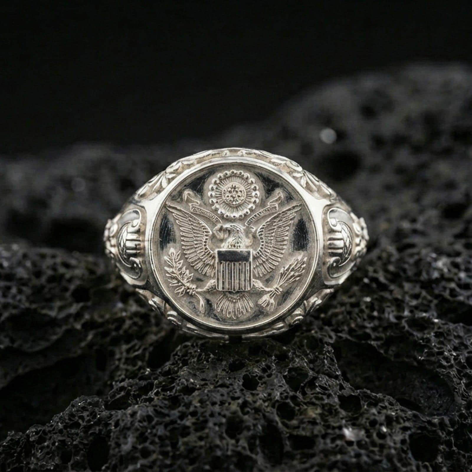 Sterling silver US eagle seal signet ring in a polished silver finish, high-relief emblem with shield and wreath details, close-up on volcanic stone