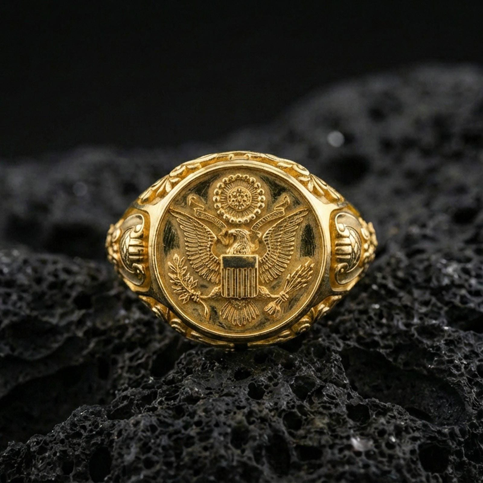 Sterling silver US eagle seal signet ring with a gold plated finish, engraved crest design with shield and laurel elements, macro on volcanic rock