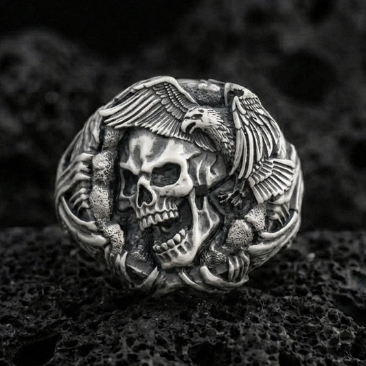 Sterling silver skull ring with an oxidized finish, eagle wings and claw details wrapping the band, macro on black volcanic rock