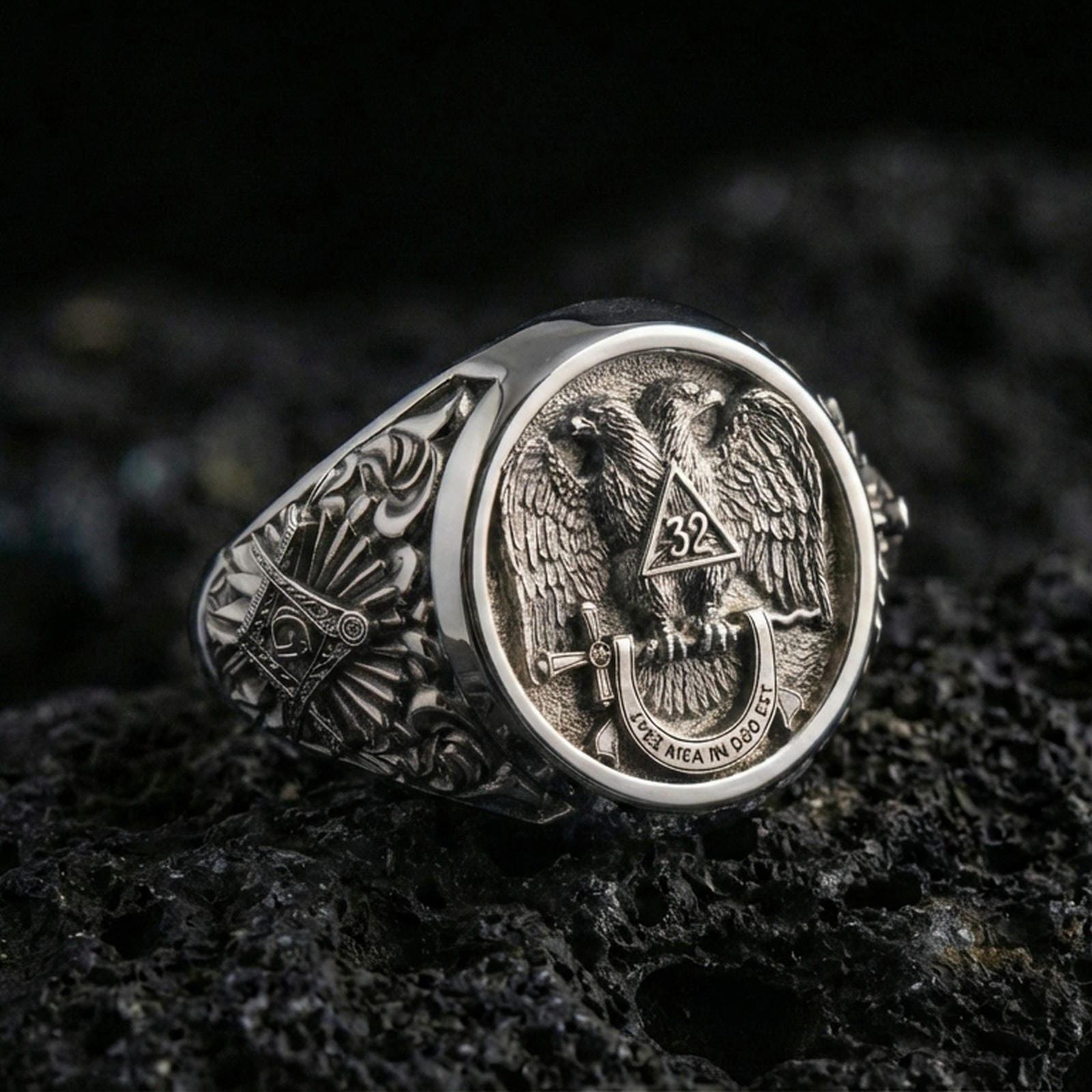 Sterling silver Masonic ring in a polished silver finish, high-relief double-headed eagle crest with ornate side engraving, close-up on volcanic stone